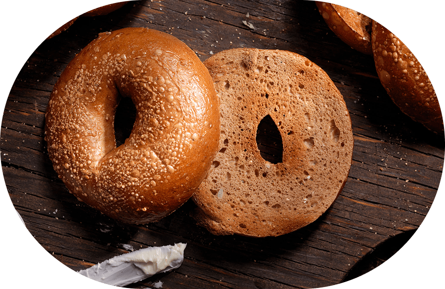 Two sesame bagels on a wooden surface.