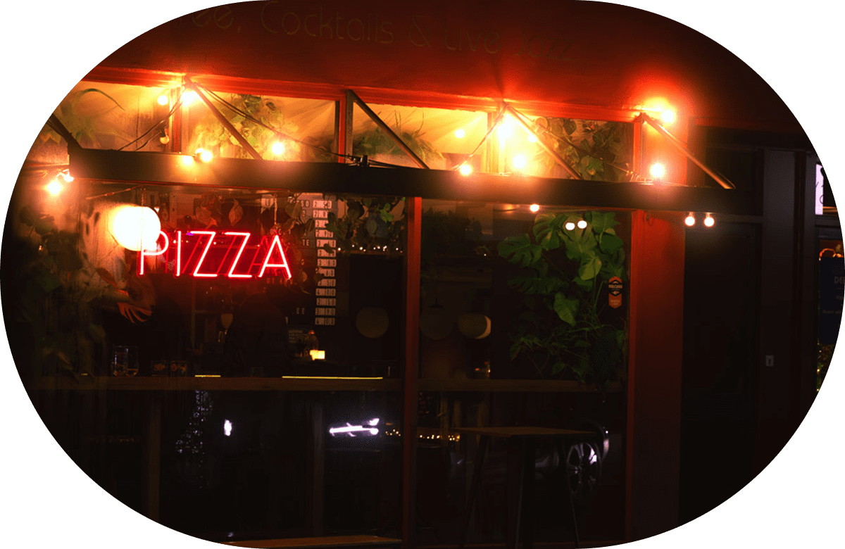 Neon pizza sign outside cozy restaurant.